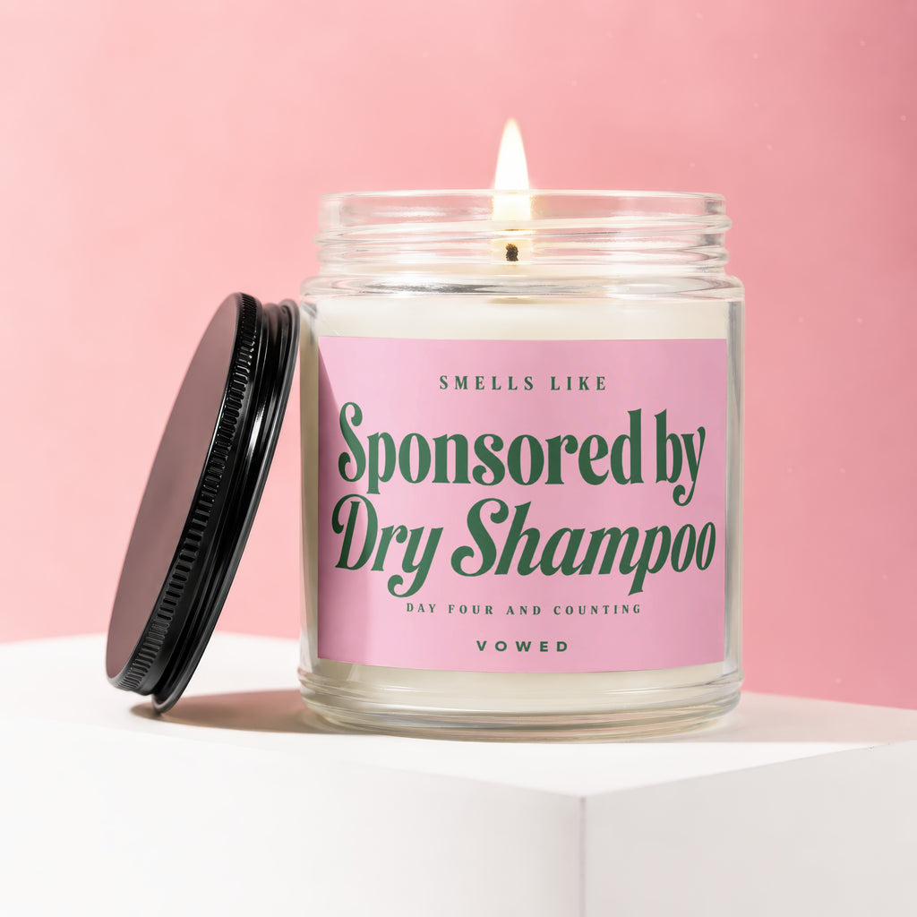Candle that says "Smells Like Sponsored by Dry Shampoo" on pink label.