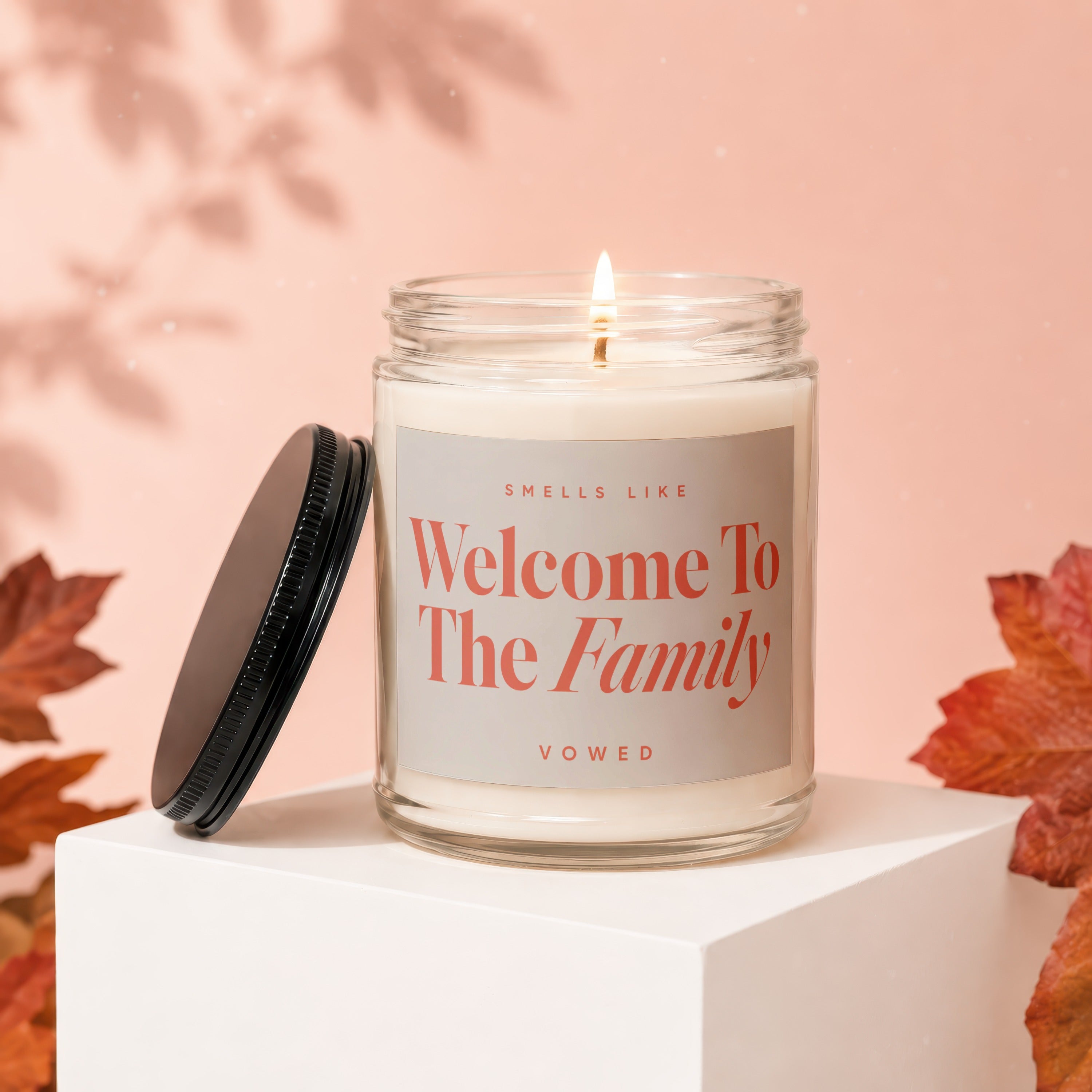 Candle with "Welcome To The Family" text, lid off, on display cube.