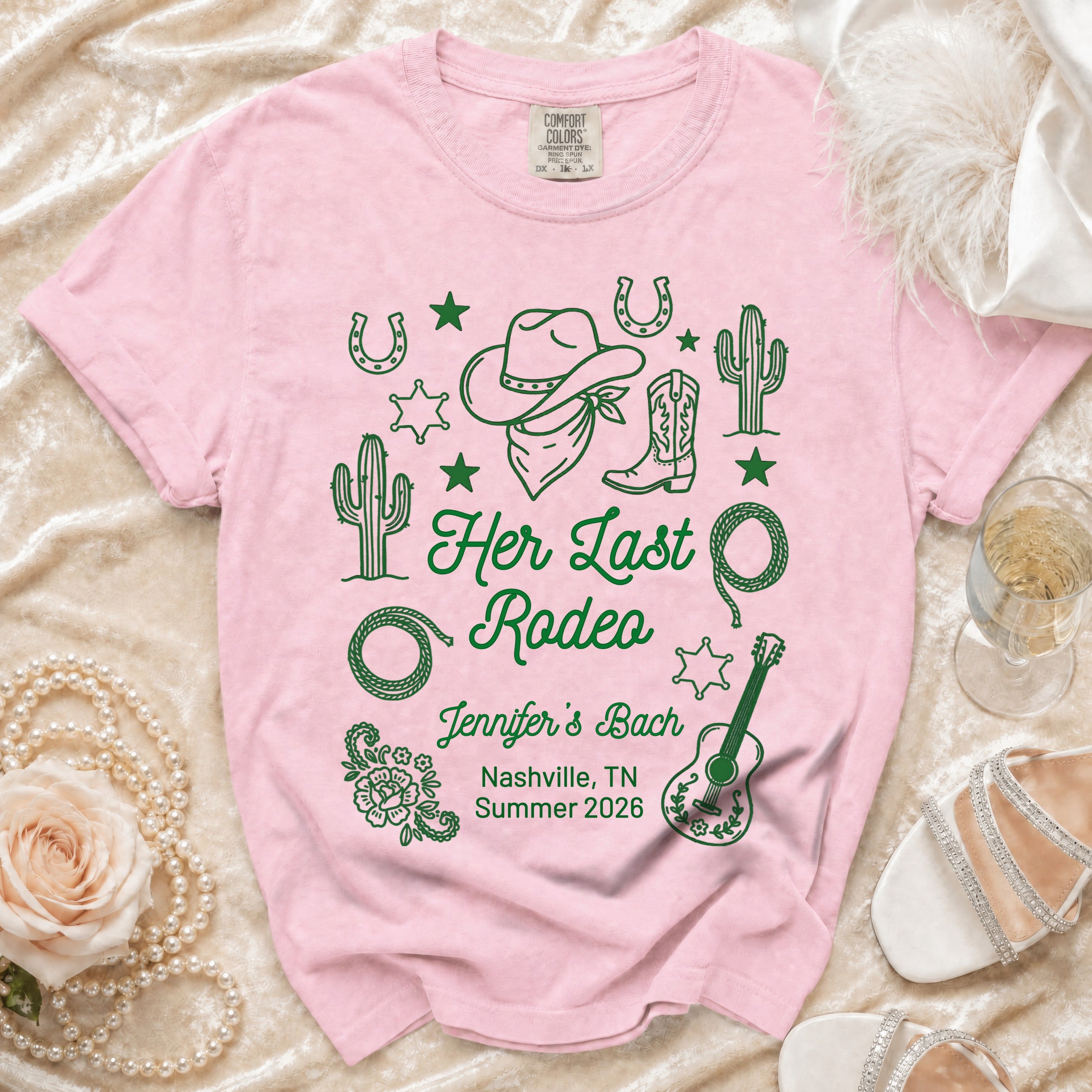 Pink t-shirt with "Her Last Rodeo" text, cowboy boots, hat, cacti, and guitar.