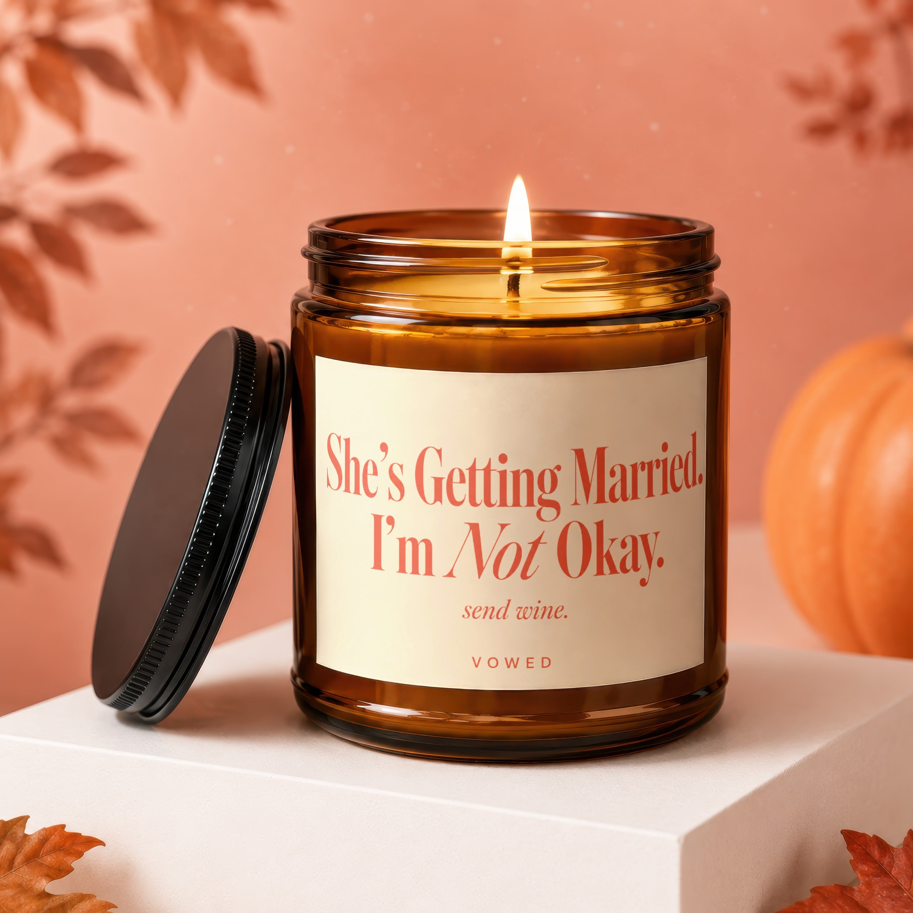 Amber candle with lit wick and label saying "She's Getting Married. I'm Not Okay. send wine."