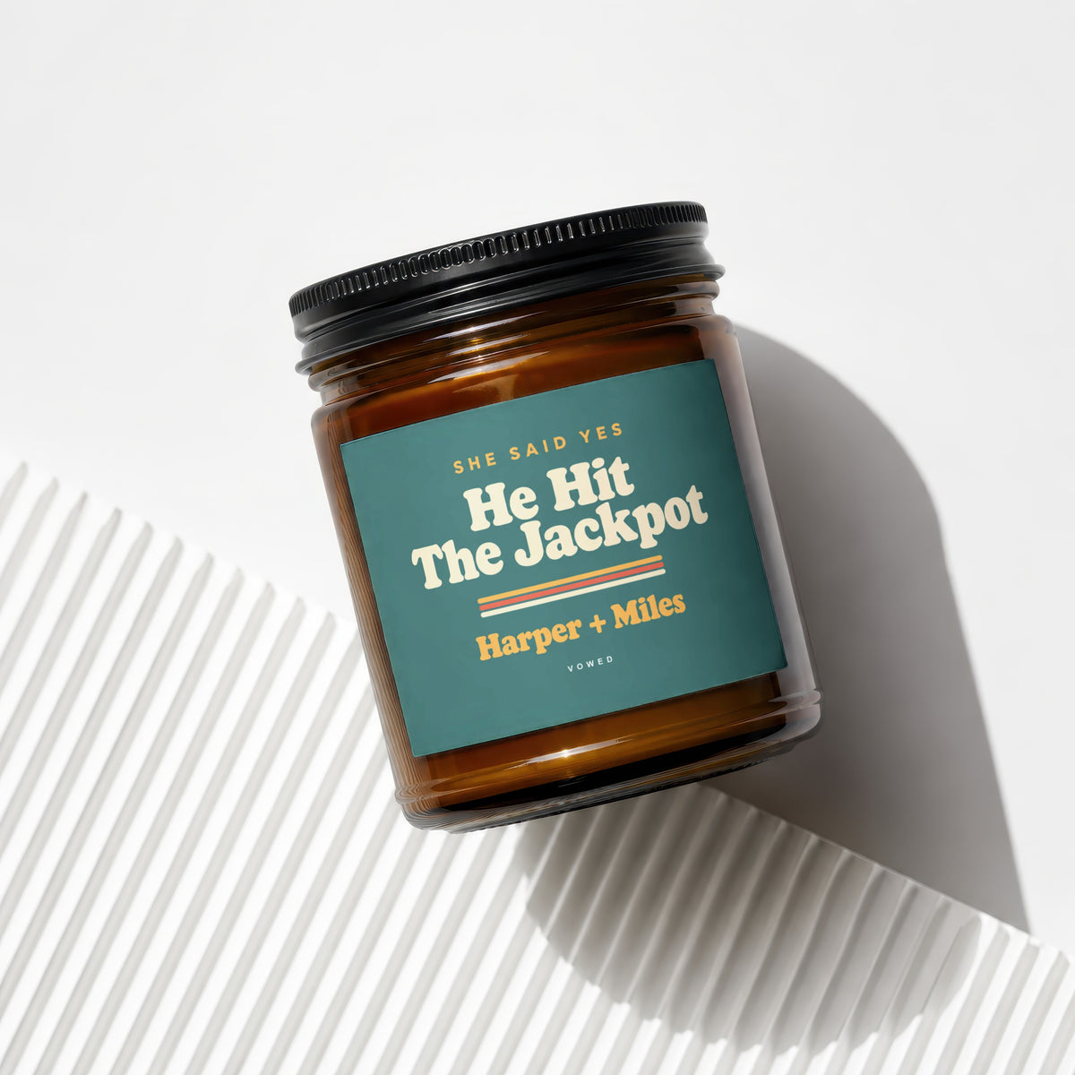 Amber jar candle with teal label reading "She Said Yes He Hit The Jackpot Harper + Miles".