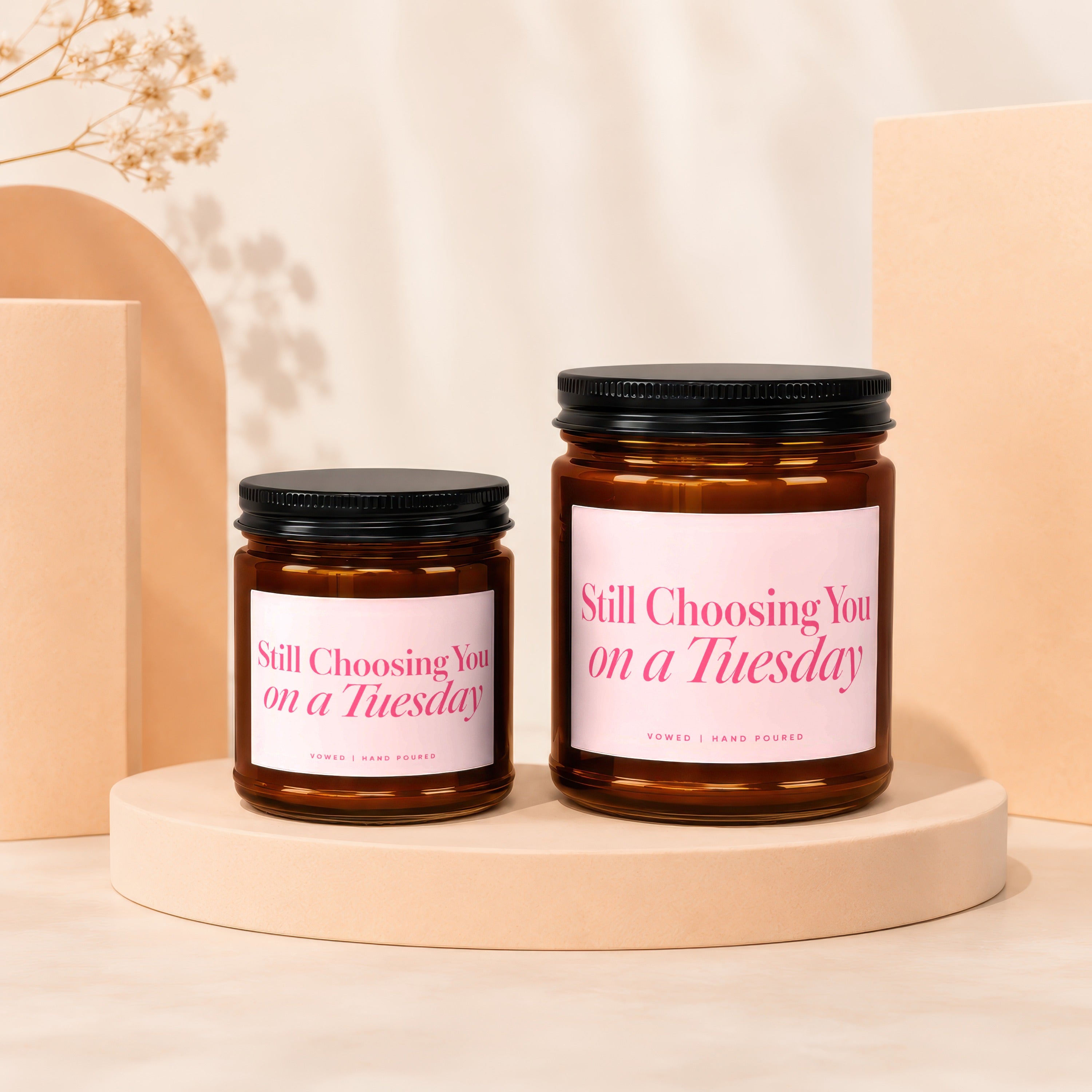 Two amber glass candles with black lids and pink labels reading "Still Choosing You on a Tuesday".