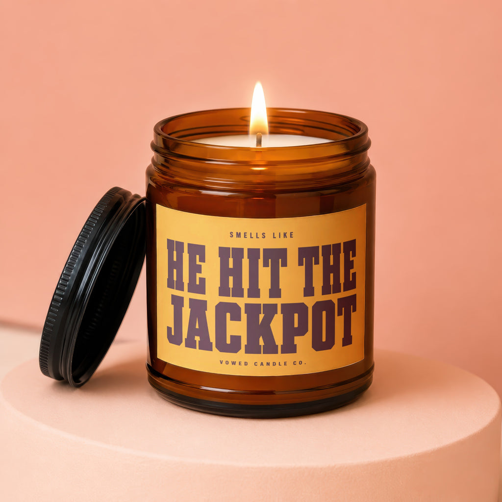 Amber jar candle lit with text "Smells Like He Hit The Jackpot".
