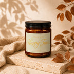 Brown glass candle with "Smells Like Happy Tears" label, on textured stone and fabric with autumn leaves.
