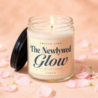 Glass jar candle with lit wick and lid, labeled "Smells Like The Newlywed Glow."