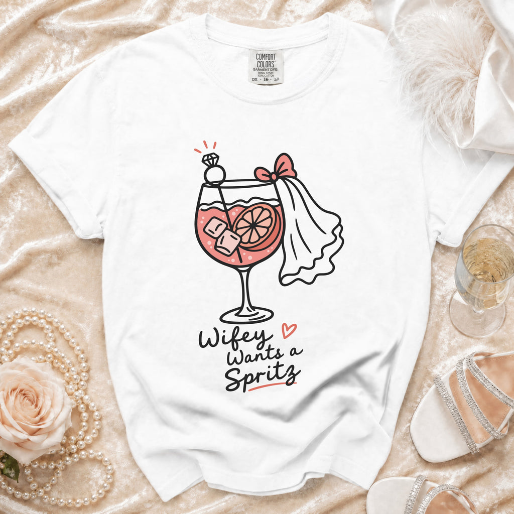 White t-shirt with a graphic of a cocktail, diamond ring, and bride's veil, reading "Wifey Wants a Spritz".