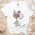 White t-shirt with a graphic of a cocktail, diamond ring, and bride's veil, reading "Wifey Wants a Spritz".