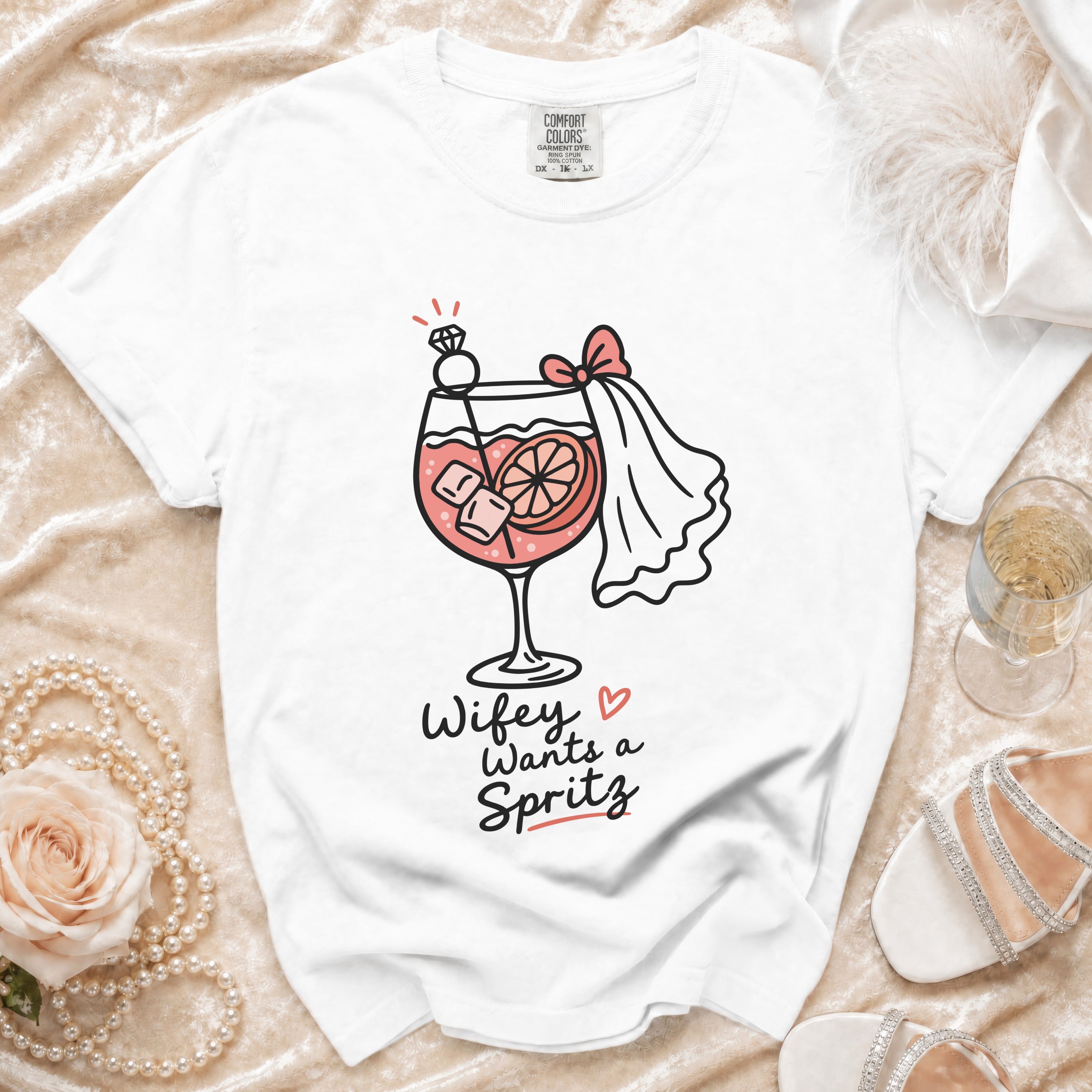 White t-shirt with a graphic of a cocktail, diamond ring, and bride's veil, reading "Wifey Wants a Spritz".