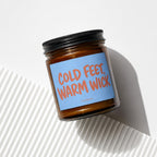 Amber glass candle with black lid, labeled "COLD FEET, WARM WICK" and "VOWED".