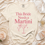 Cream t-shirt with pink text "This Bride Needs a Martini" and martini glass graphic.