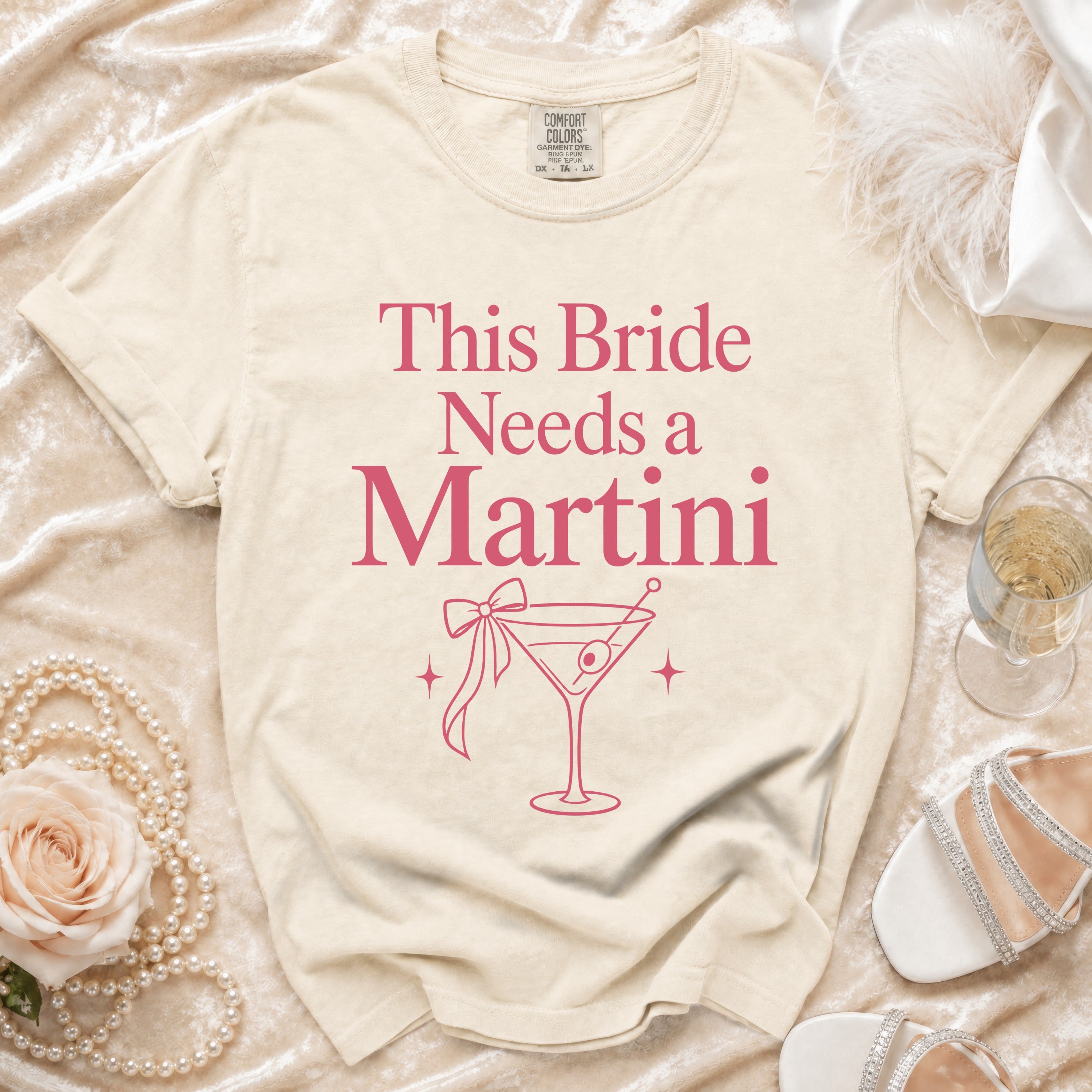 Cream t-shirt with pink text "This Bride Needs a Martini" and martini glass graphic.