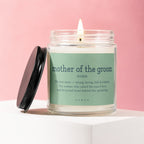 Glass candle with lit wick and black lid, labeled "mother of the groom noun."