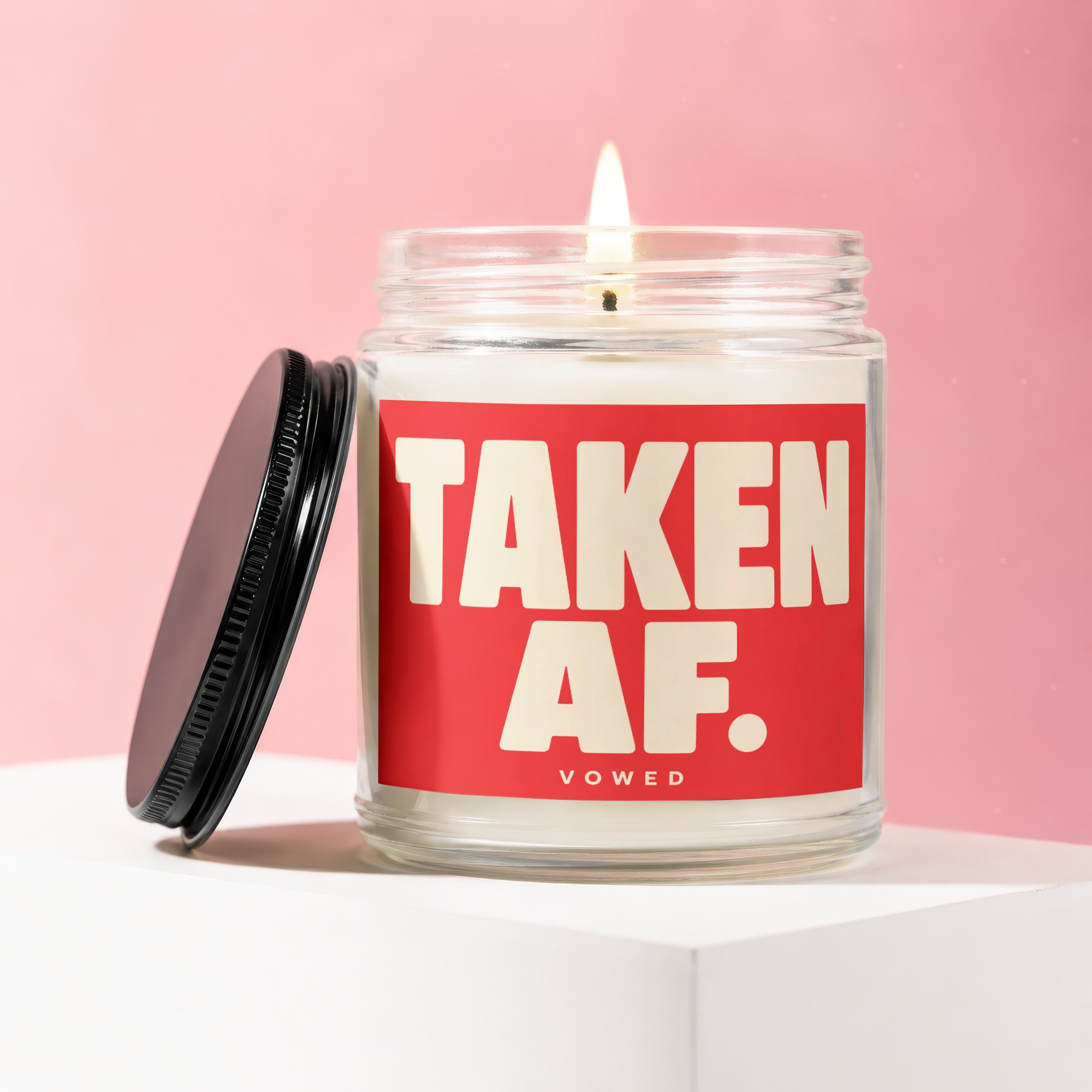 Candle with a lit wick and a black lid, featuring "TAKEN AF." text.