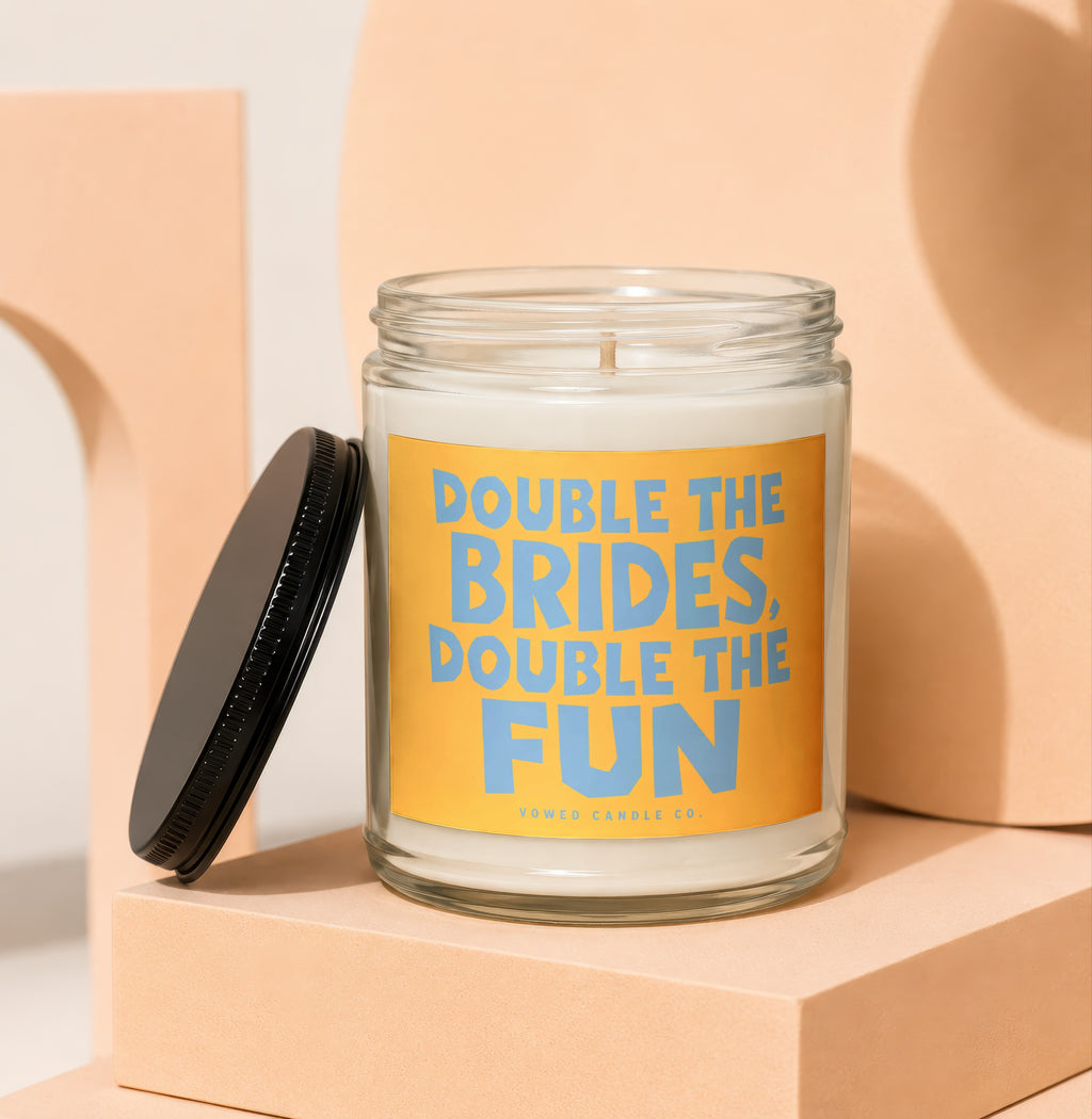 Glass candle with orange label reading "DOUBLE THE BRIDES, DOUBLE THE FUN".