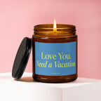 Lit amber glass candle with a blue label that reads "Love You. Need a Vacation. VOWED."