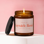 Brown glass candle with lit flame and black lid. Label reads "Gaywatch: Married".