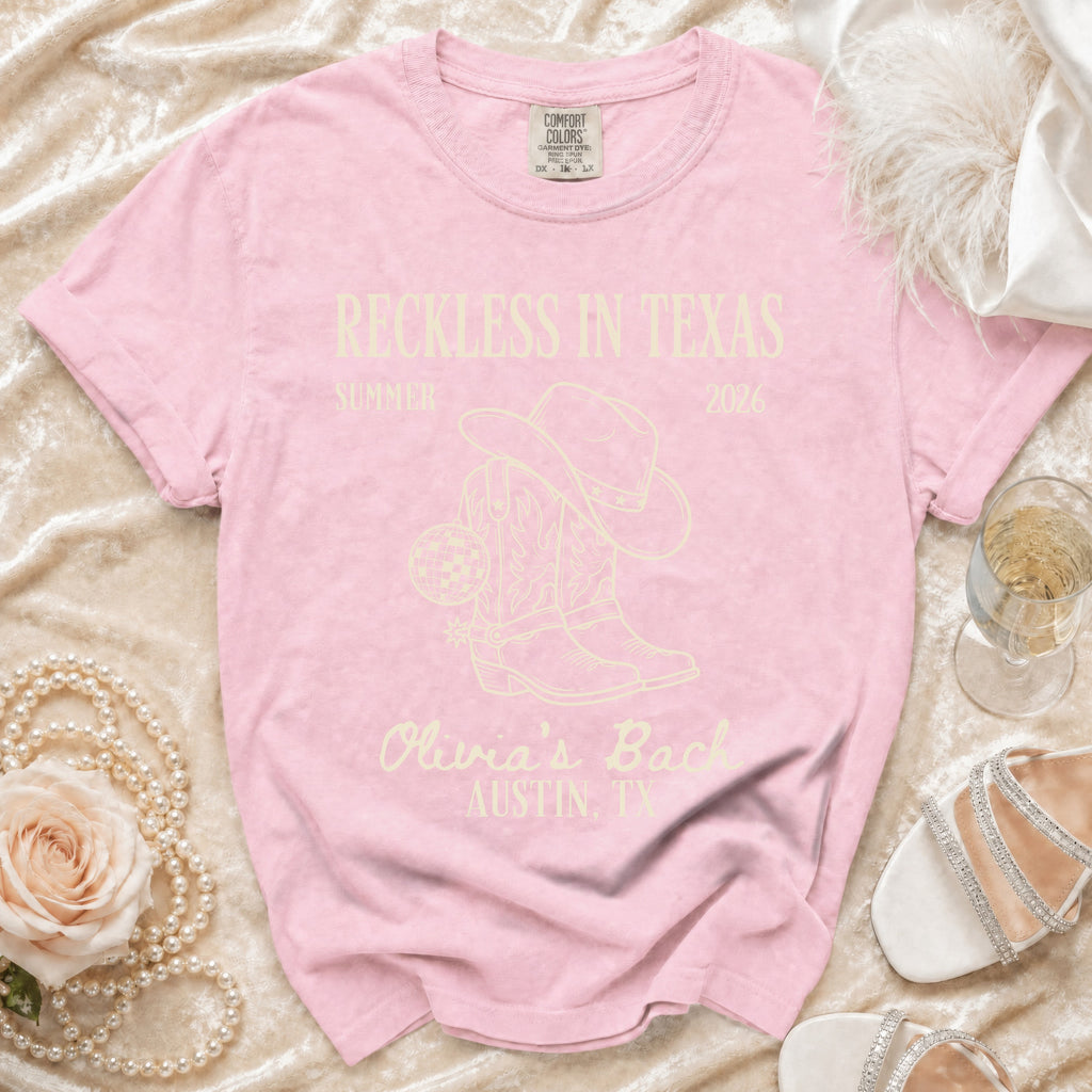 Pink t-shirt with "Reckless in Texas" and cowboy boots graphic.