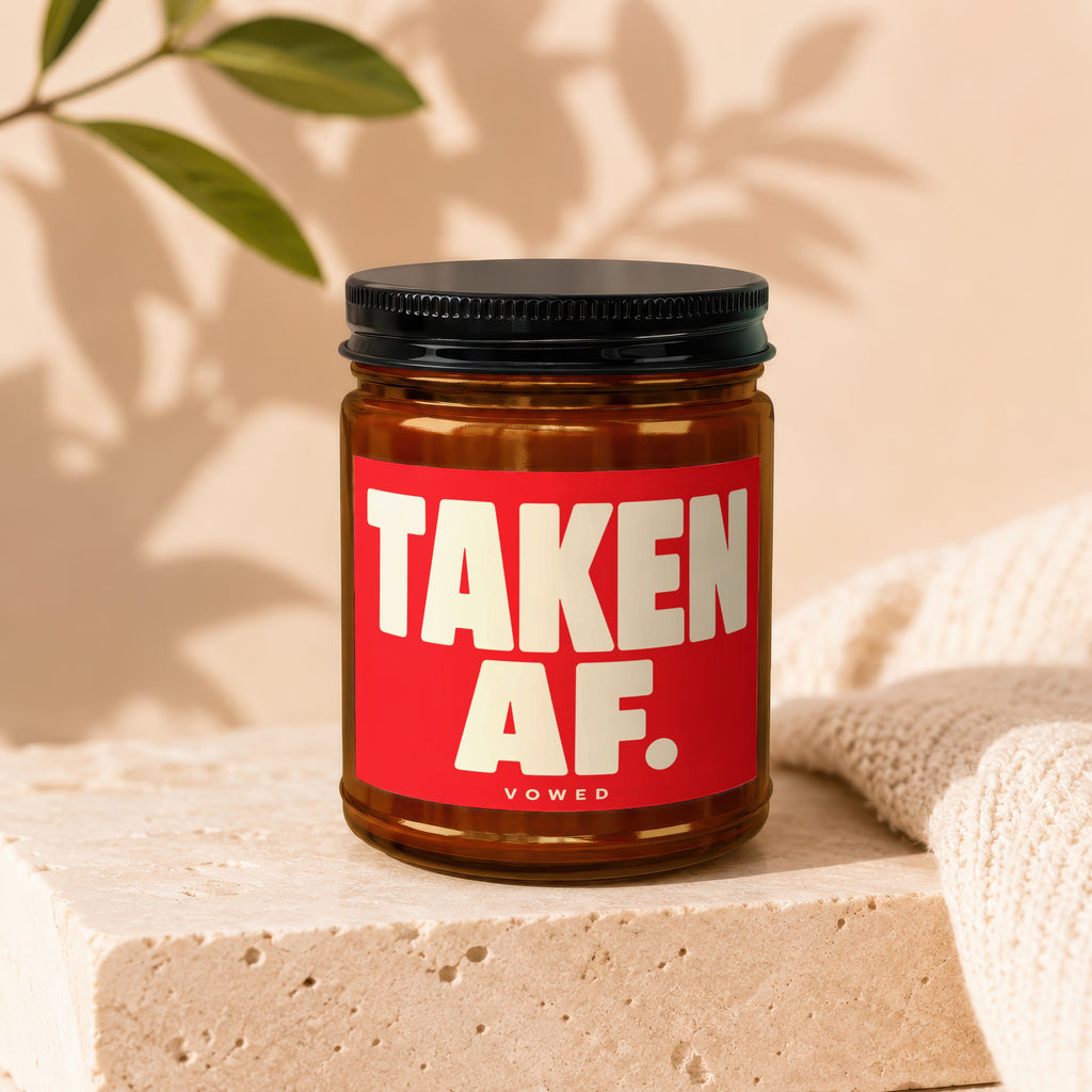 Amber jar candle with black lid, red label reads "TAKEN AF. VOWED".