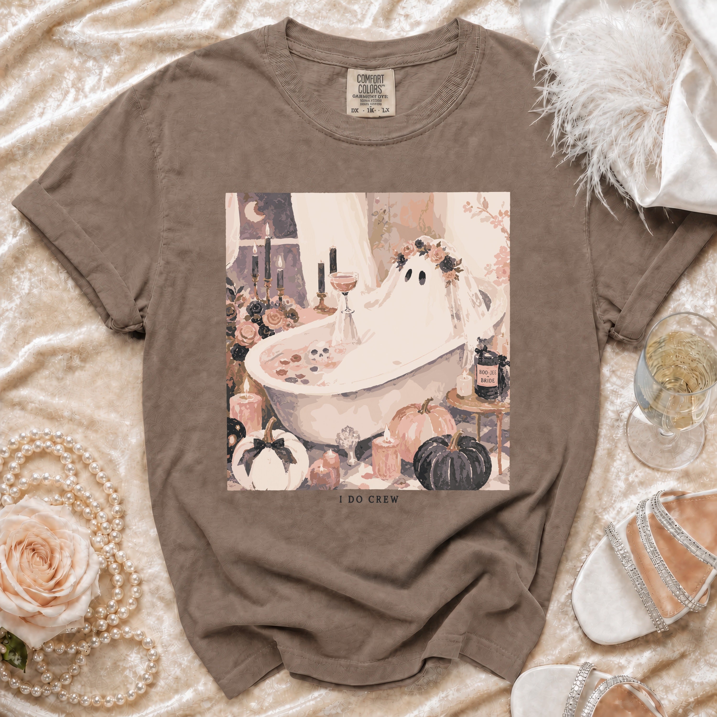 Brown crewneck t-shirt featuring a pastel Halloween illustration of a ghost in a bathtub, surrounded by pumpkins, candles, and flowers, with text reading I DO CREW.