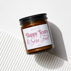 Amber jar candle with black lid reads "Smells Like Happy Tears & Sore Feet Vowed".