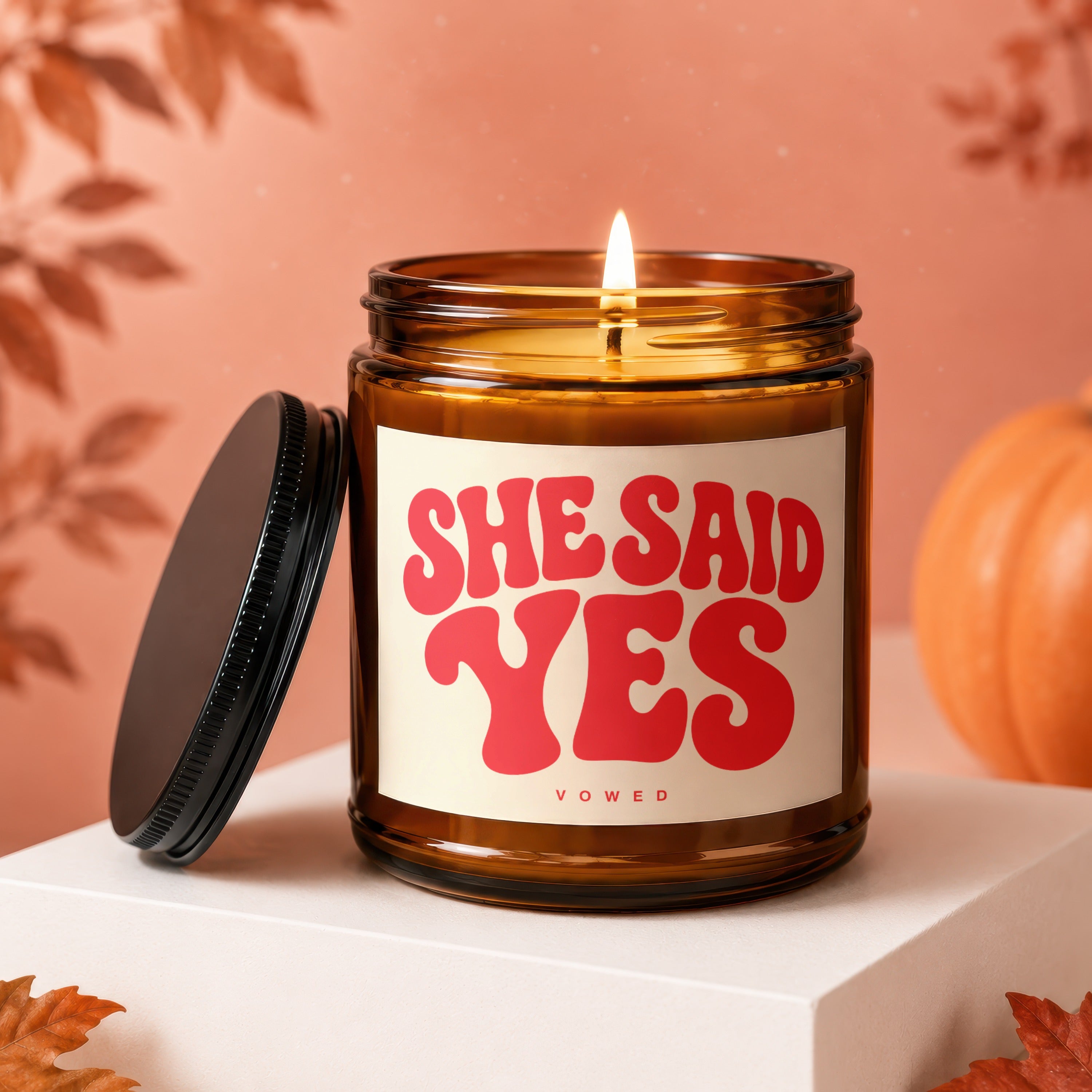 Amber jar candle with lit flame, "SHE SAID YES" text, and "VOWED" subtitle.