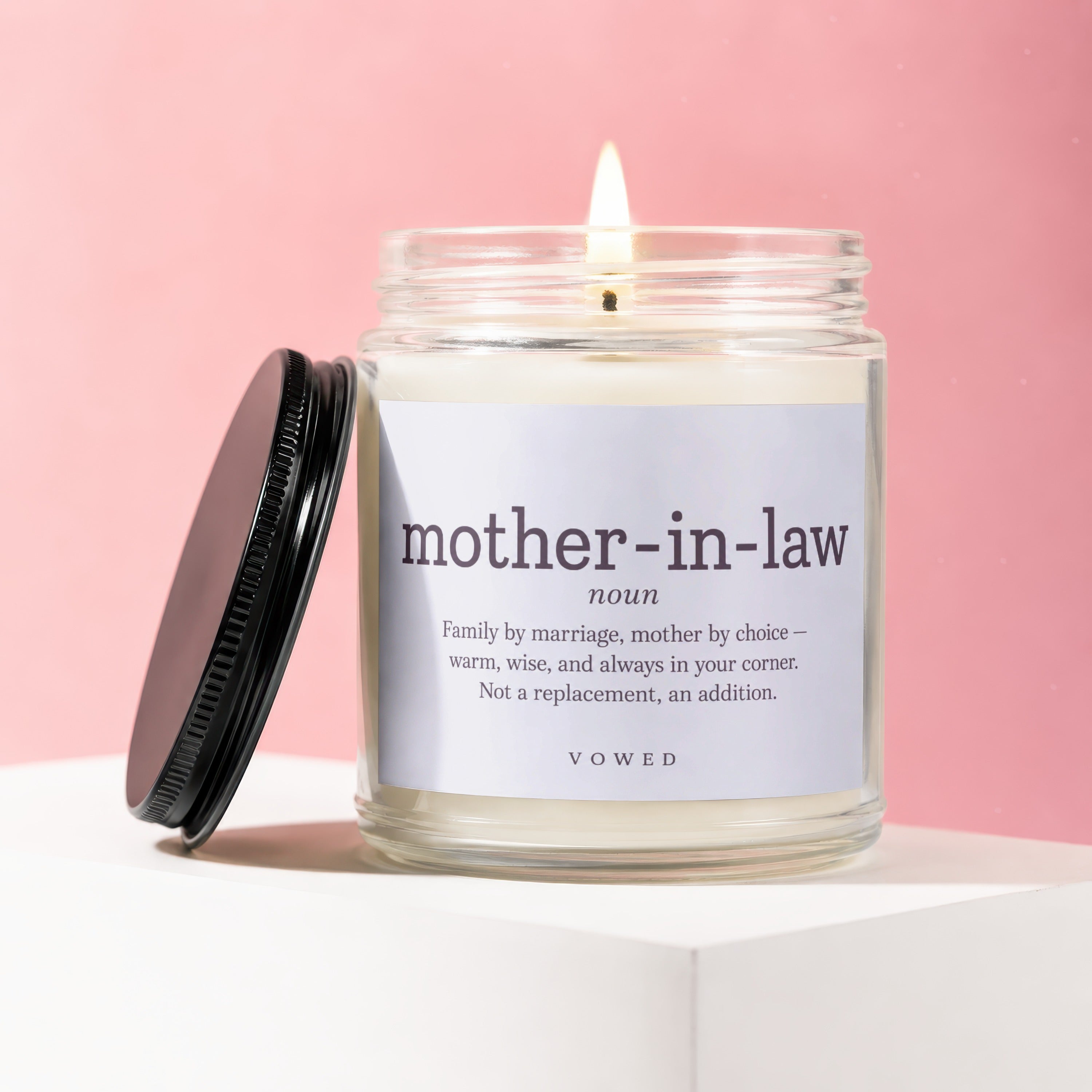 Glass candle with a lit wick and a label defining "mother-in-law".