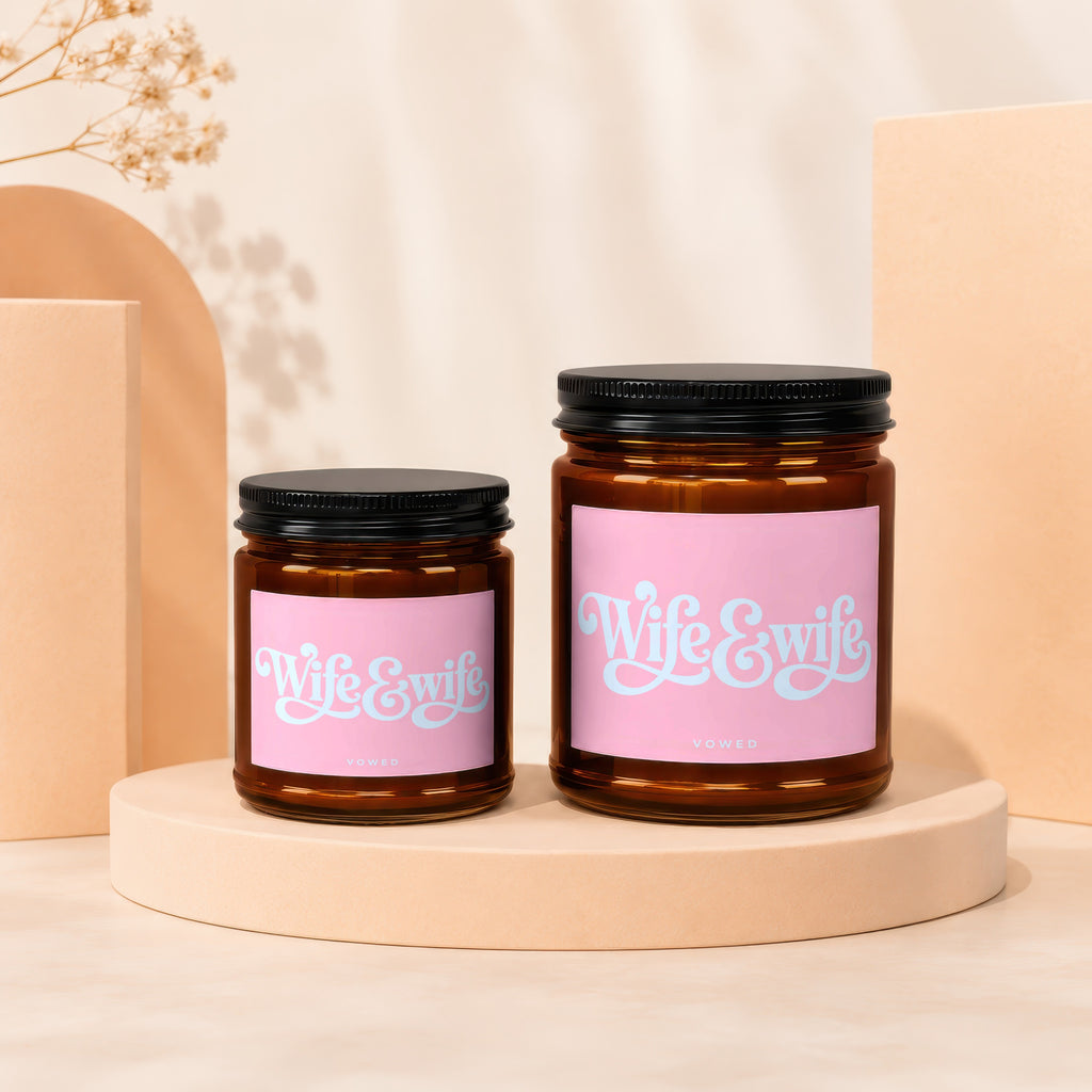 Two amber glass candles with pink labels reading "Wife & Wife" and "VOWED".