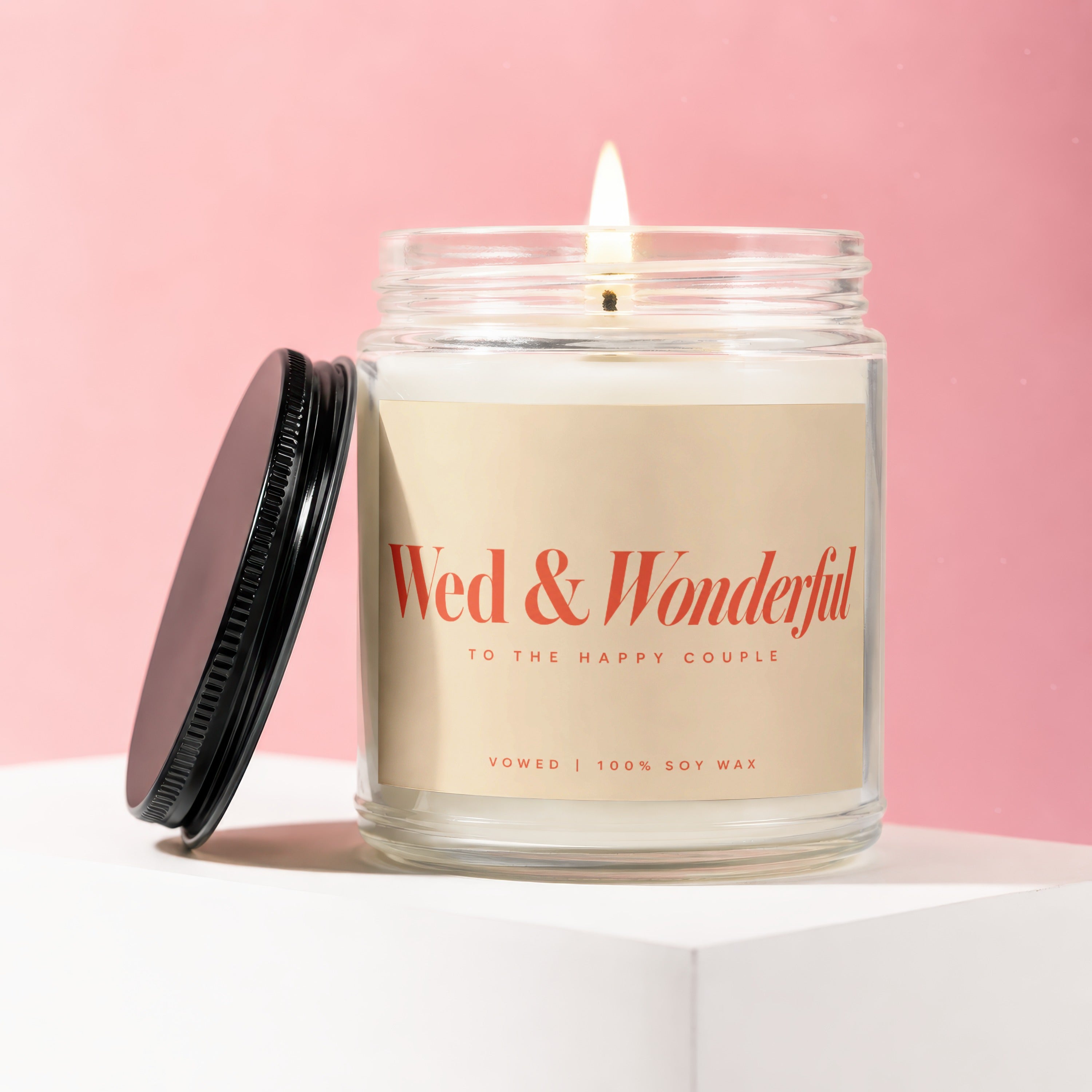 Glass jar candle with lit wick, label reads "Wed & Wonderful To The Happy Couple Vowed 100% Soy Wax".