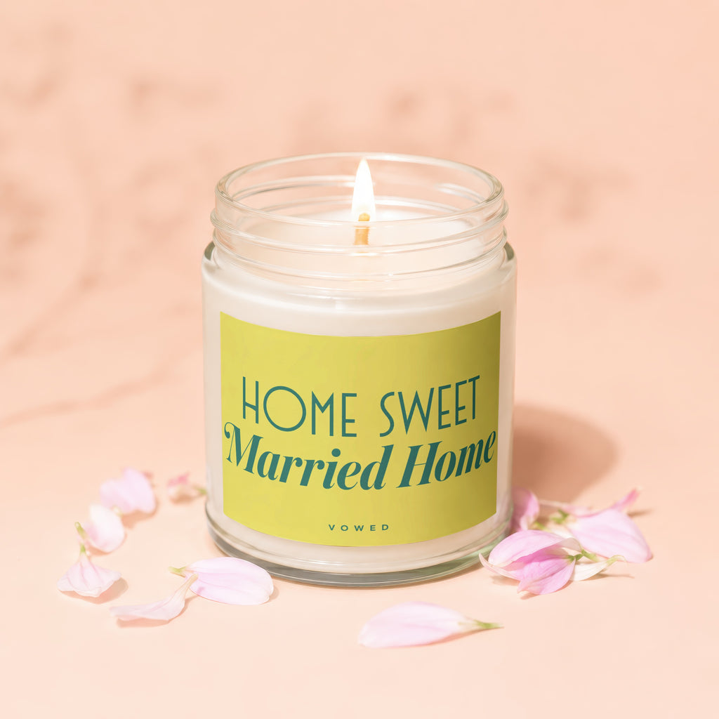 Candle with "Home Sweet Married Home" text on a yellow label, surrounded by pink petals.