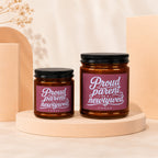 Two brown glass candles with black lids and white text labels reading "Proud parent of a newlywed."