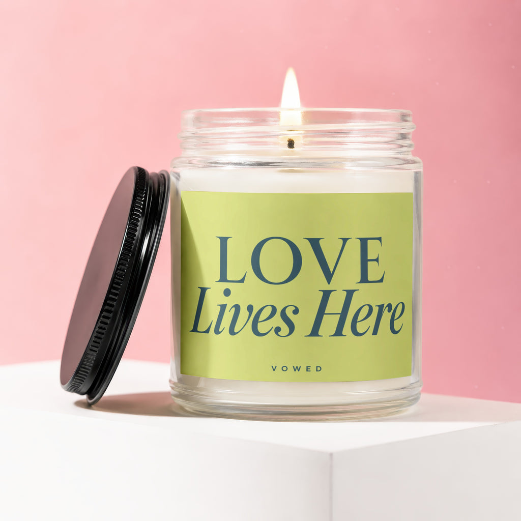 Lit candle in glass jar with lime green label that reads "LOVE Lives Here VOWED".