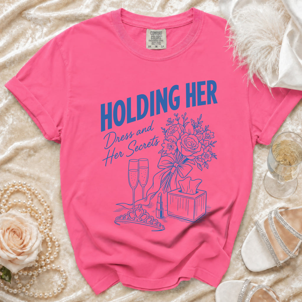 Pink t-shirt with "HOLDING HER Dress and Her Secrets" text and themed illustration.