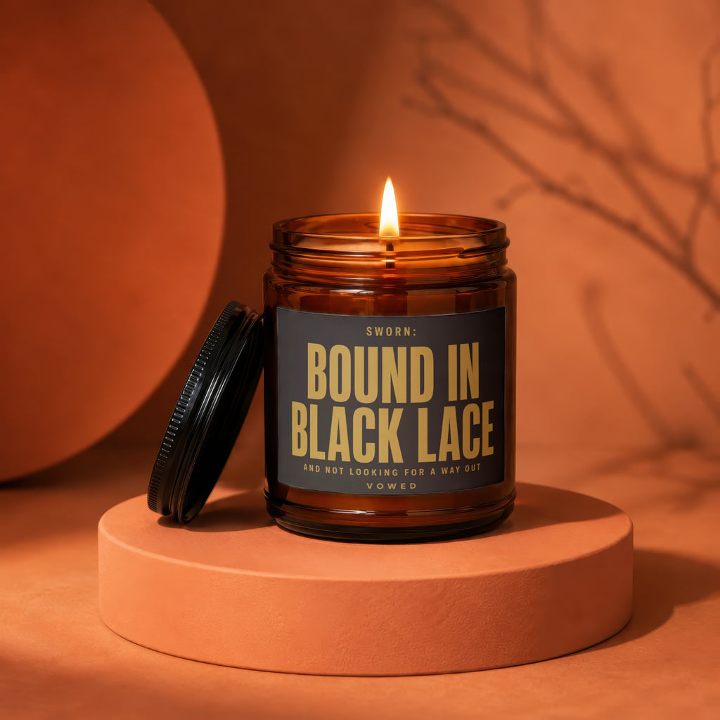 Brown glass candle with lit flame and black label "SWORN: BOUND IN BLACK LACE".