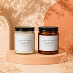 Two candles with black lids and white labels reading "YOU HAVE BEEN CHOSEN TO HOLD MY BOUQUET, MY PHONE, AND MY COMPOSURE".