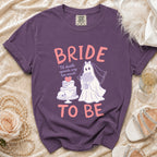 Purple t-shirt with "BRIDE TO BE" and ghost bride with cake and skull graphic.