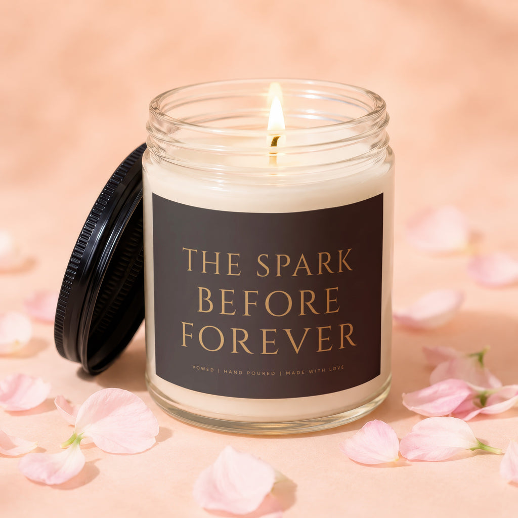 Glass candle with black lid, labeled "The Spark Before Forever".