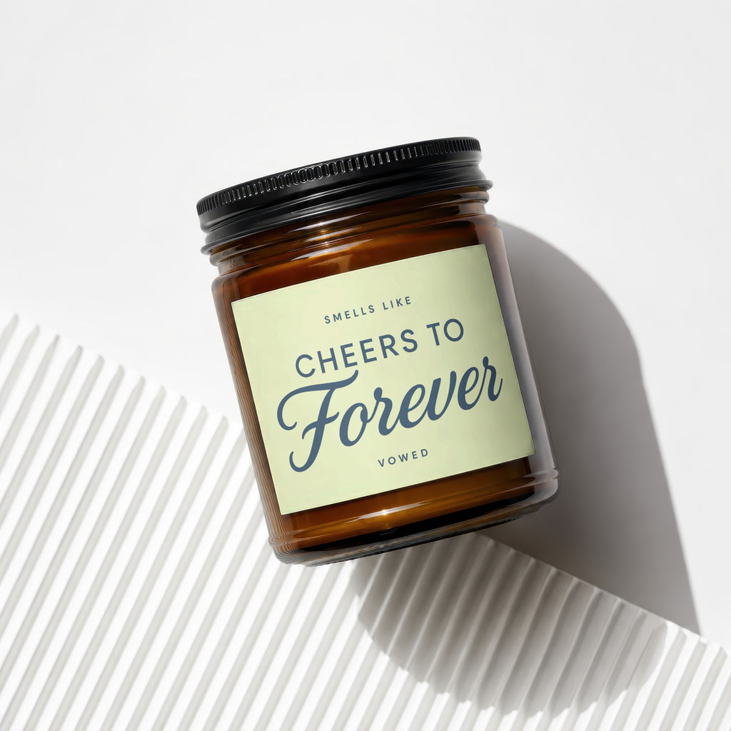 Amber jar candle with black lid, cream label reads "SMELLS LIKE CHEERS TO Forever VOWED".