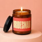 Brown glass candle with burning wick, red label reading BRIDESMAID, VOWED.