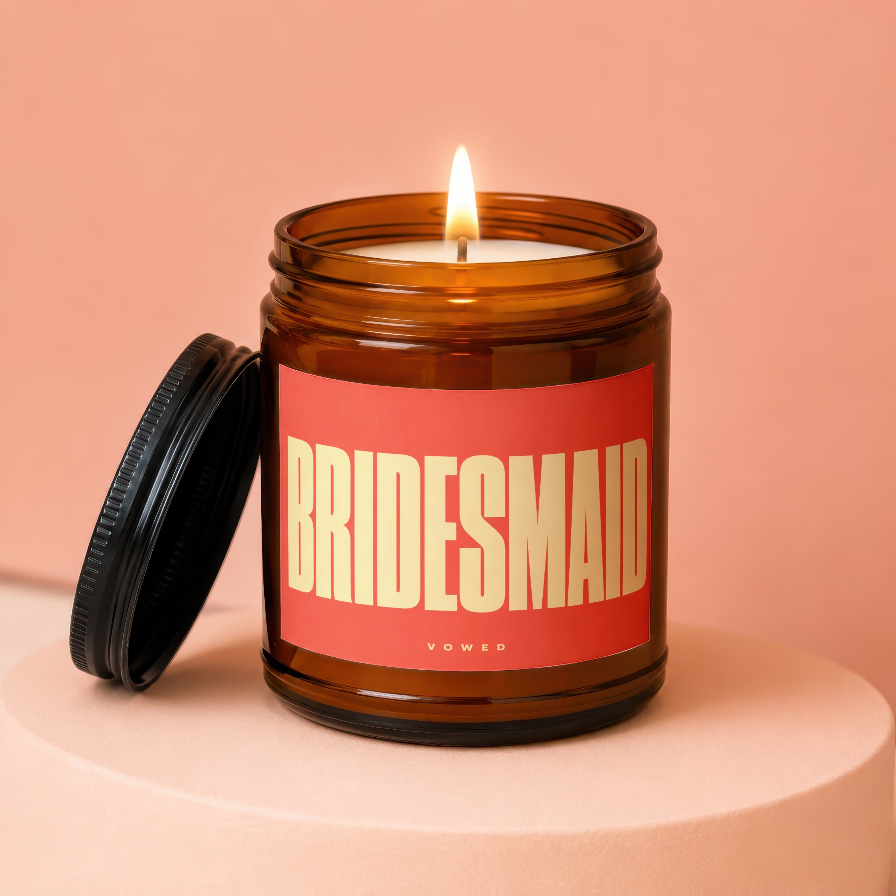 Brown glass candle with burning wick, red label reading BRIDESMAID, VOWED.