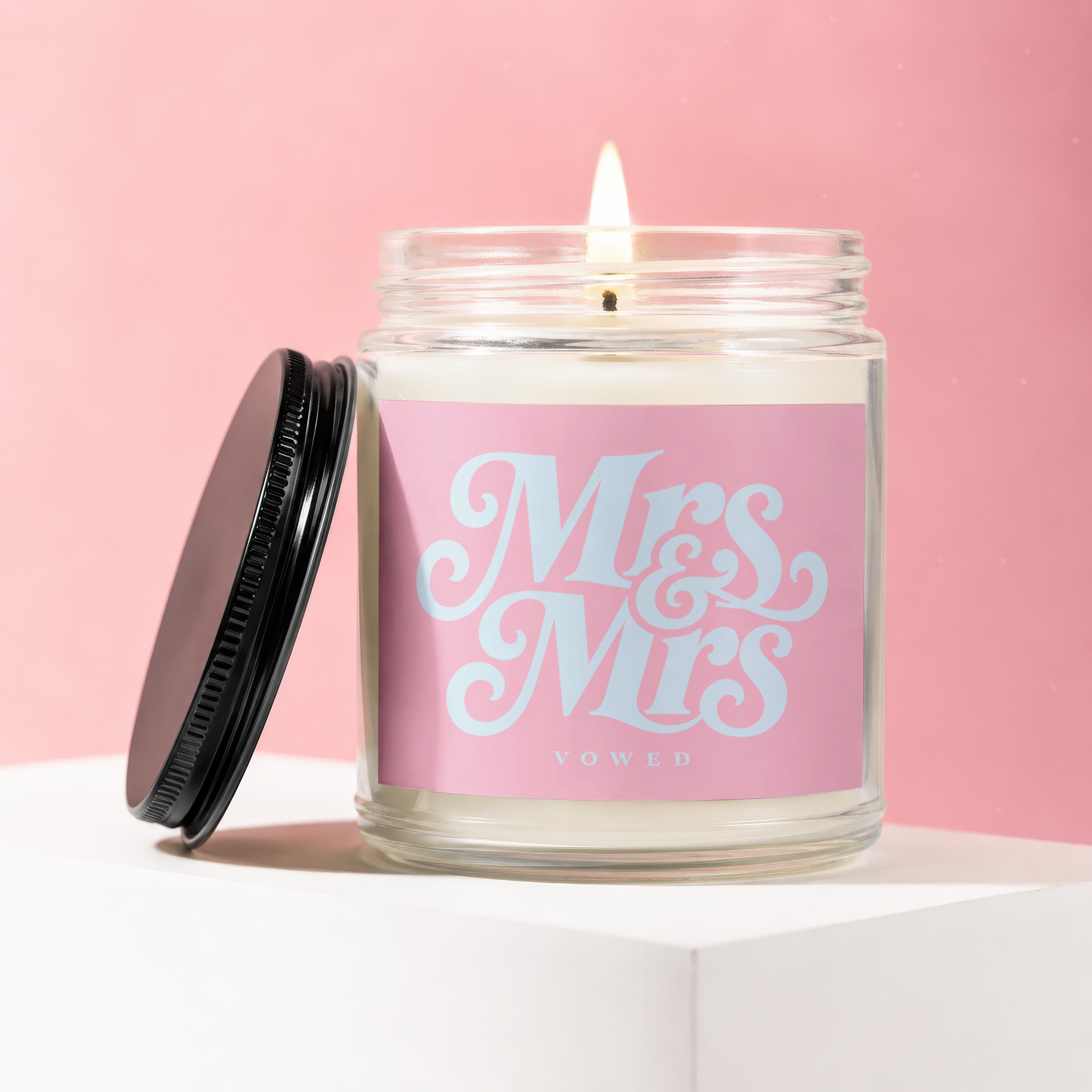 Lit candle in glass jar with pink label that says "Mrs & Mrs VOWED".