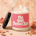 Lit candle in a glass jar with a pink label reading "the odd perfect pair."