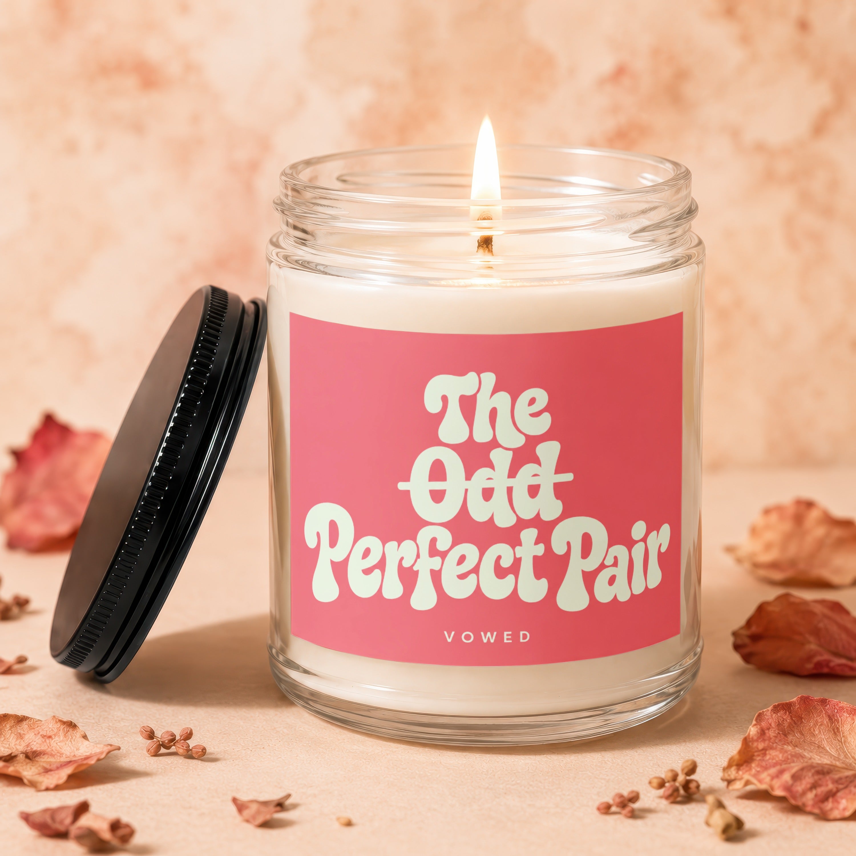 Lit candle in a glass jar with a pink label reading "the odd perfect pair."