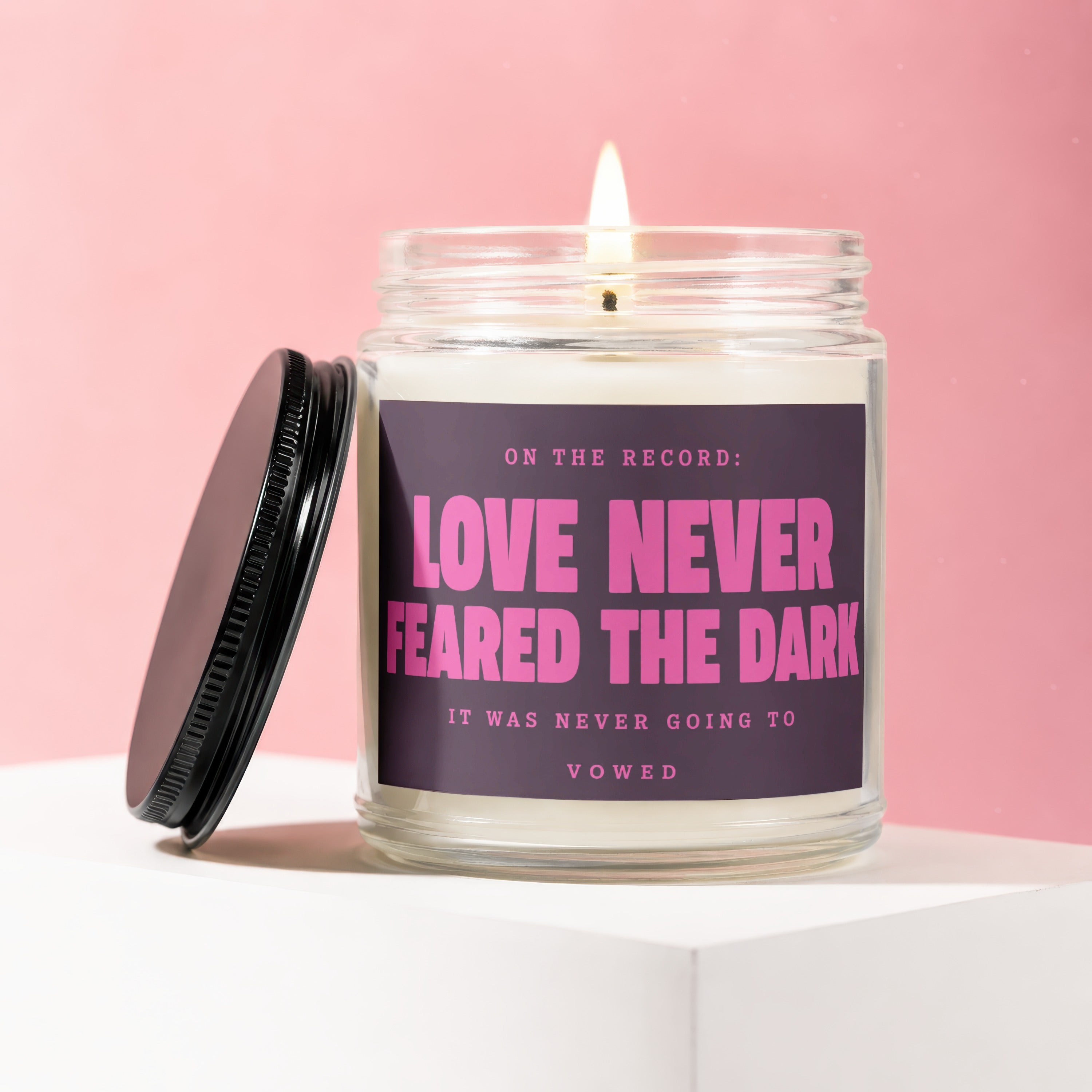 Lit candle with black lid, text "Love Never Feared the Dark" on purple label.