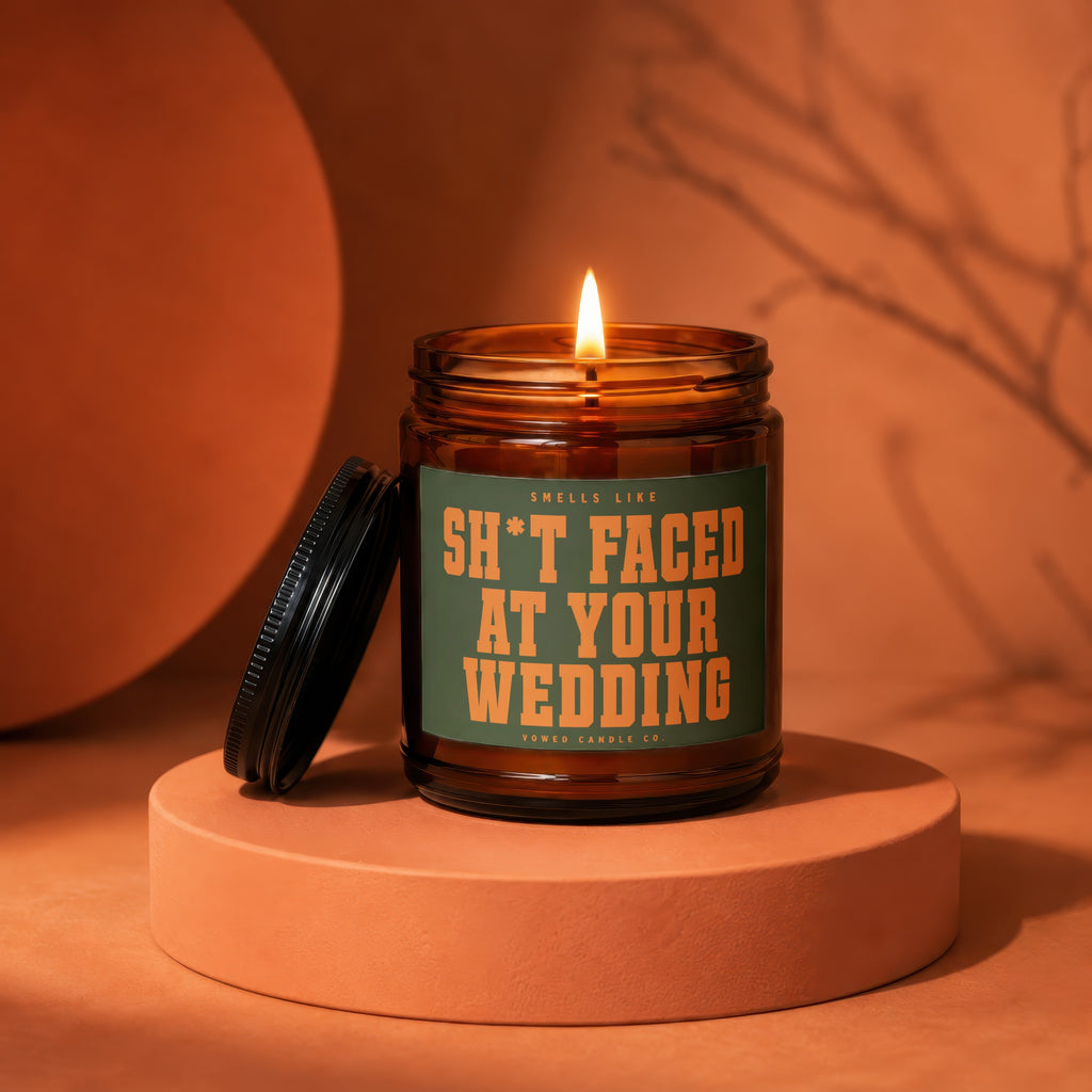 Lit amber candle with label "Smells Like Sh*t Faced At Your Wedding".