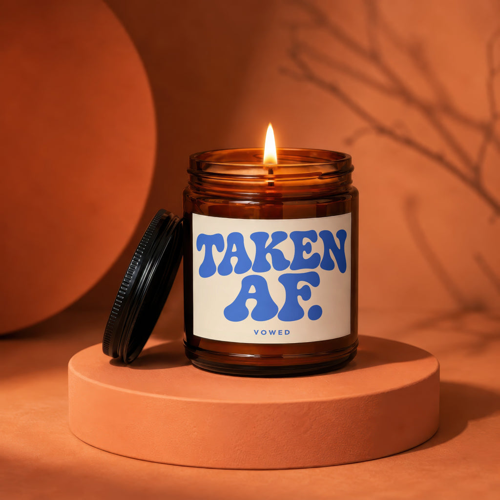 Amber jar candle with lit wick and black lid, reads "TAKEN AF. VOWED".
