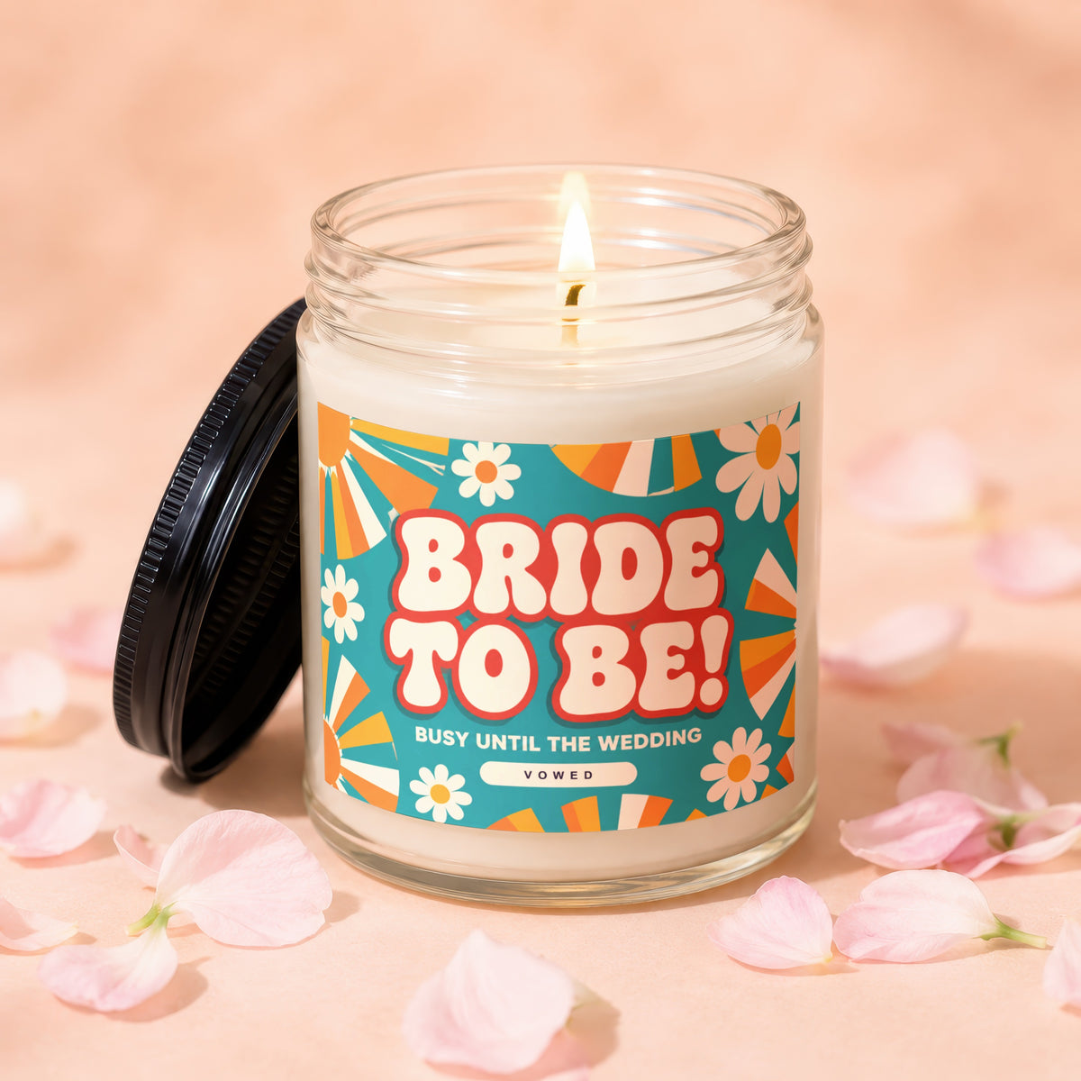 Glass jar candle with a lit wick and "Bride To Be!" label, surrounded by petals.