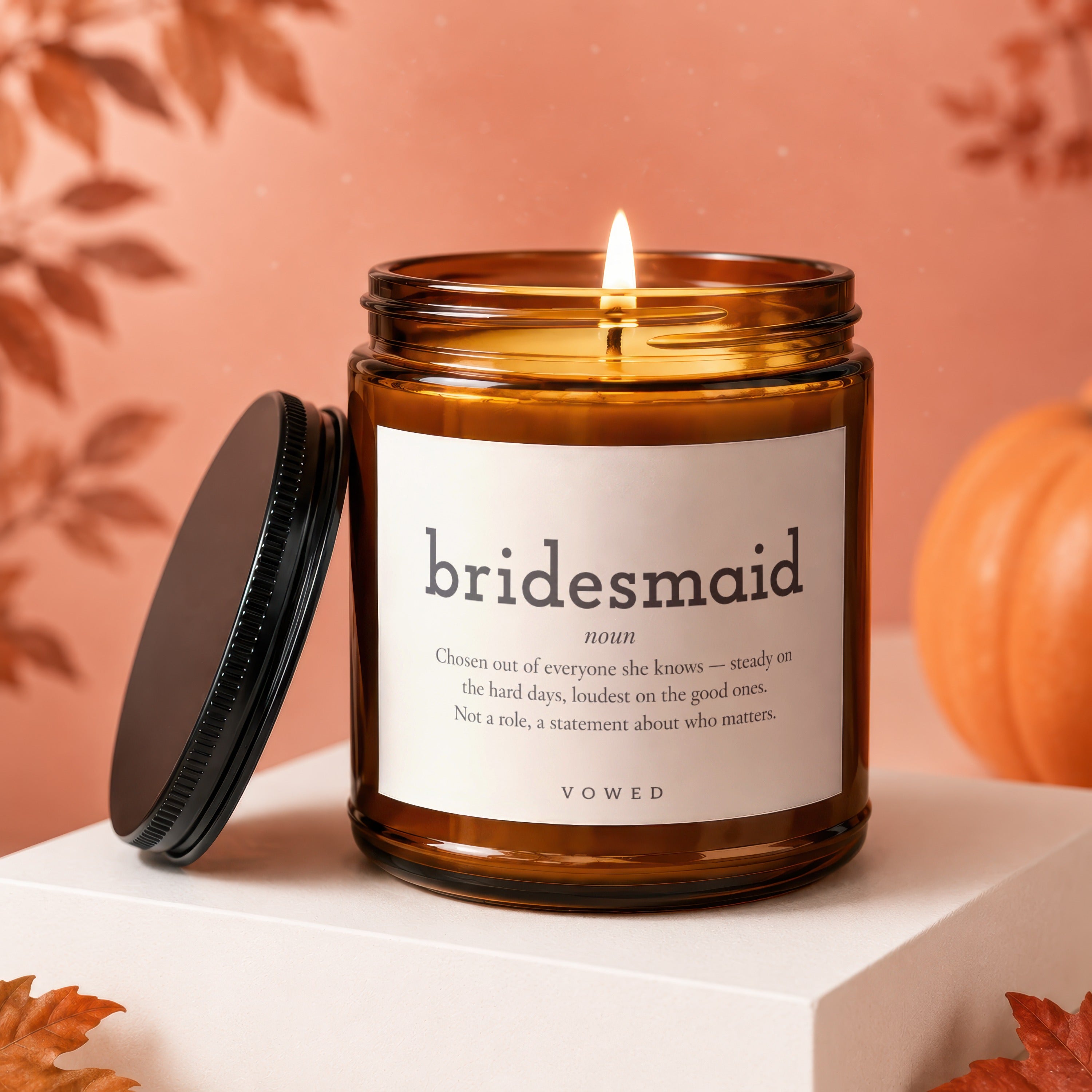 A lit bridesmaid candle in a amber jar with definition text and fall decor.