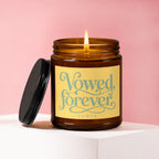 Amber jar candle with lit wick and black lid, reads "Vowed, forever VOWED".