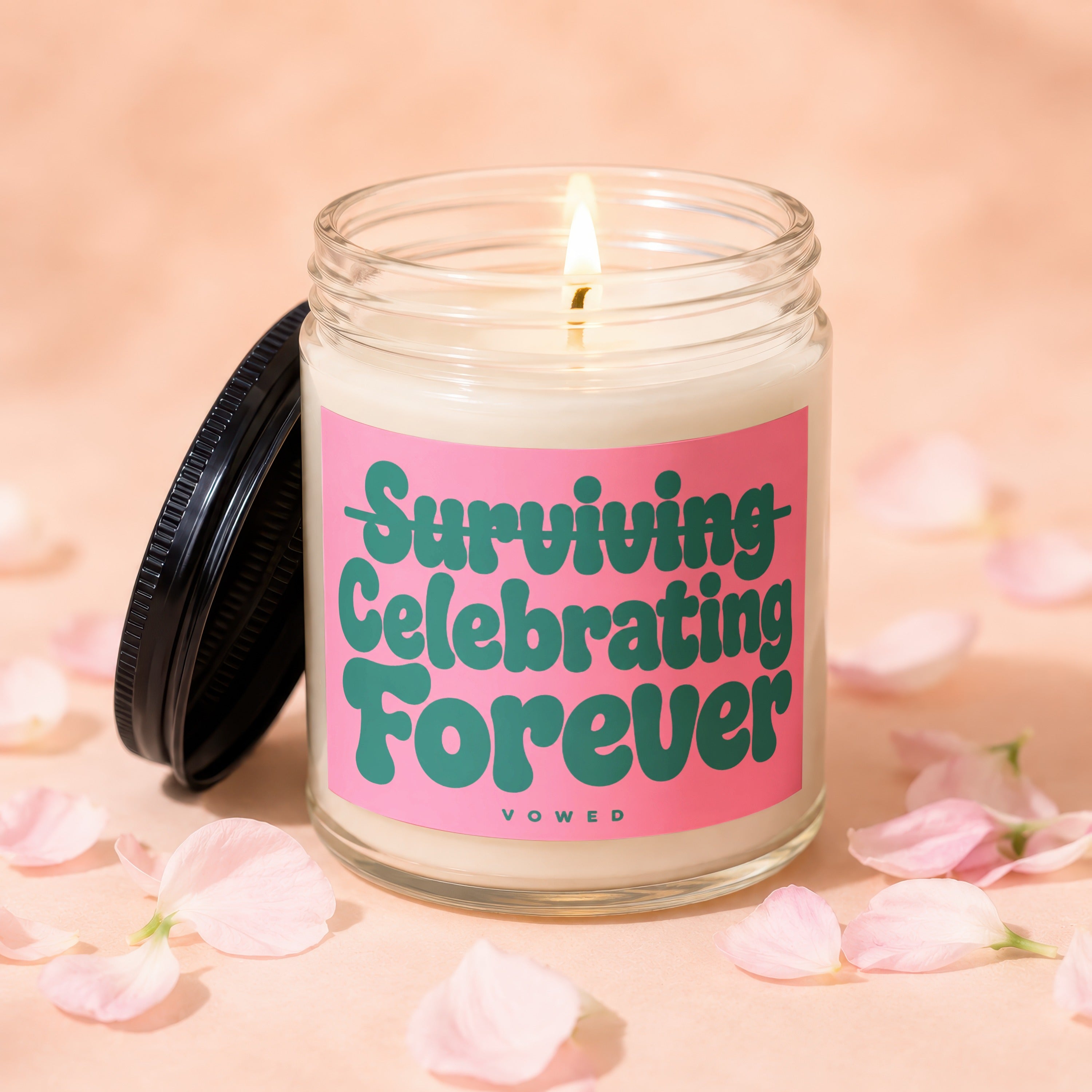 Lit glass candle with pink label reading "Surviving Celebrating Forever".