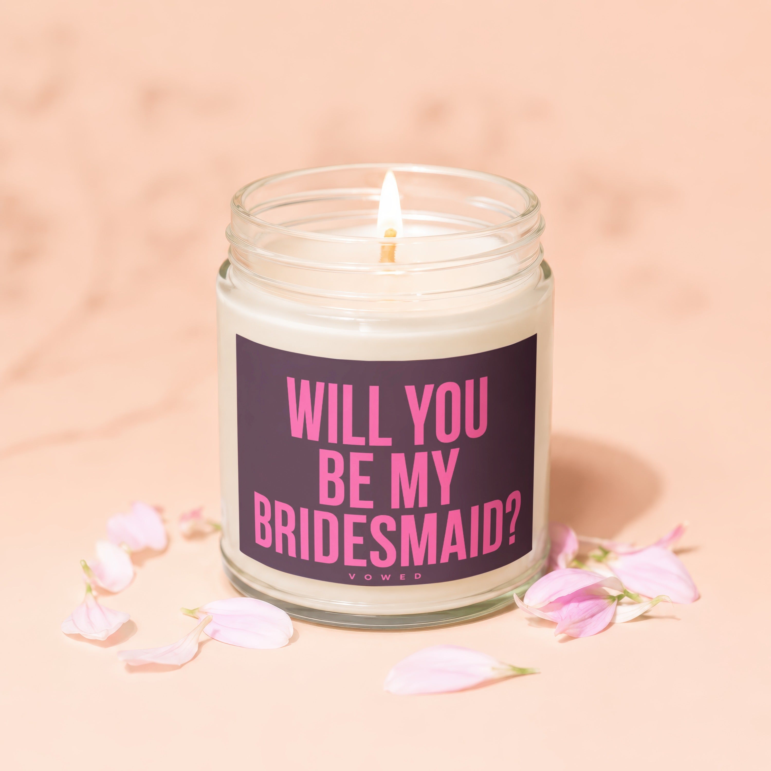 Glass candle with lit wick and "Will You Be My Bridesmaid?" text on label.